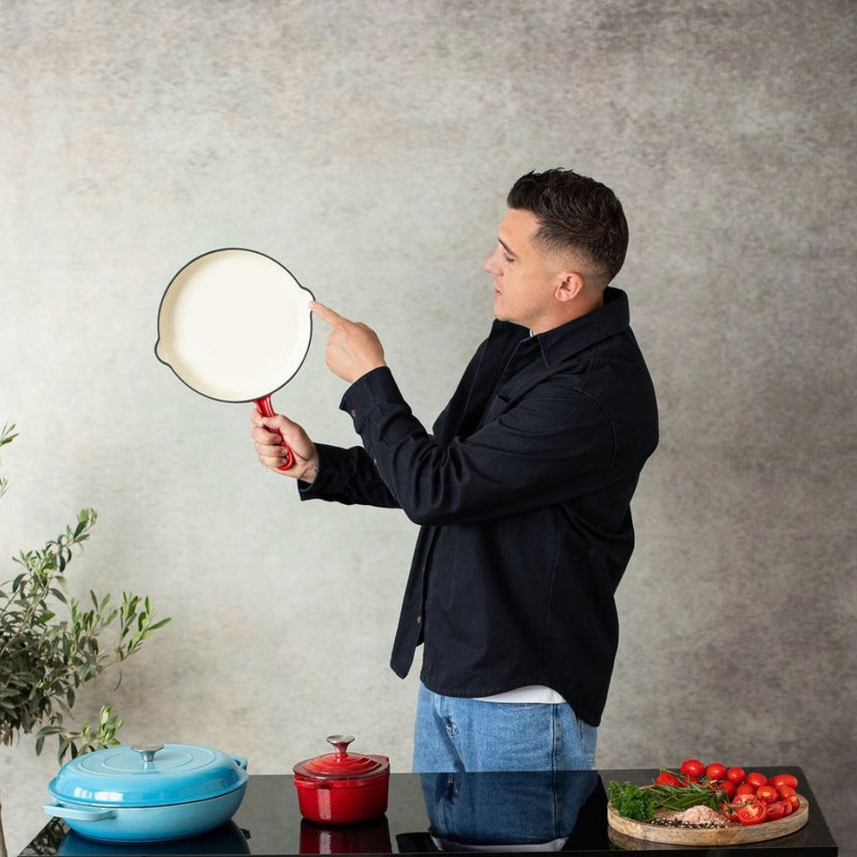 Man holding a frying pan in a kitchen setting with cookware and ingredients on a table.